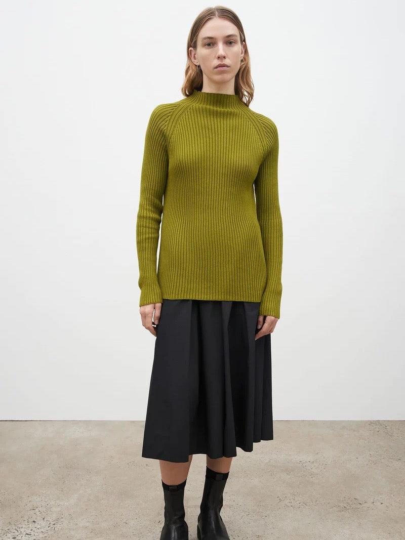 A woman wearing a green Row Top - Lawn sweater and black skirt.