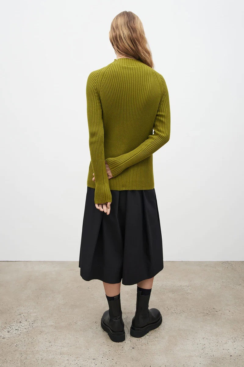 The back view of a woman wearing a Kowtow green turtleneck sweater and black skirt.
