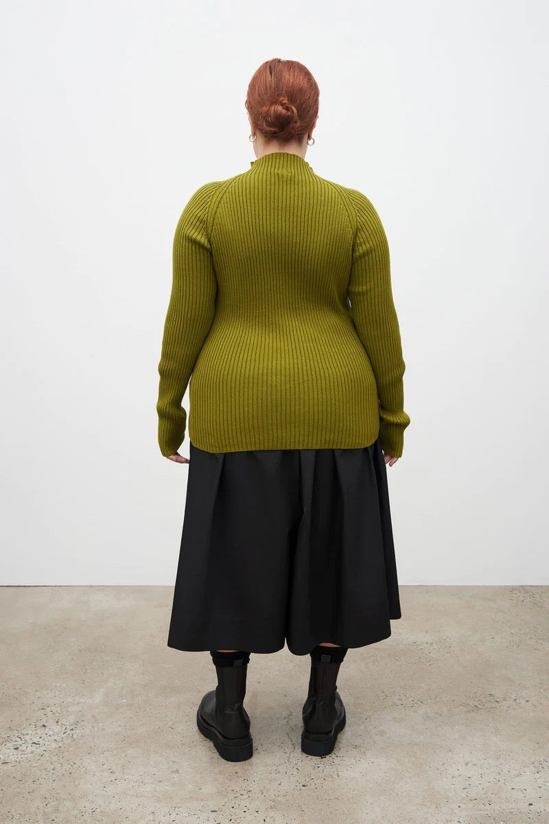 A woman wearing a green &quot;Row Top - Lawn&quot; sweater by Kowtow and black skirt.