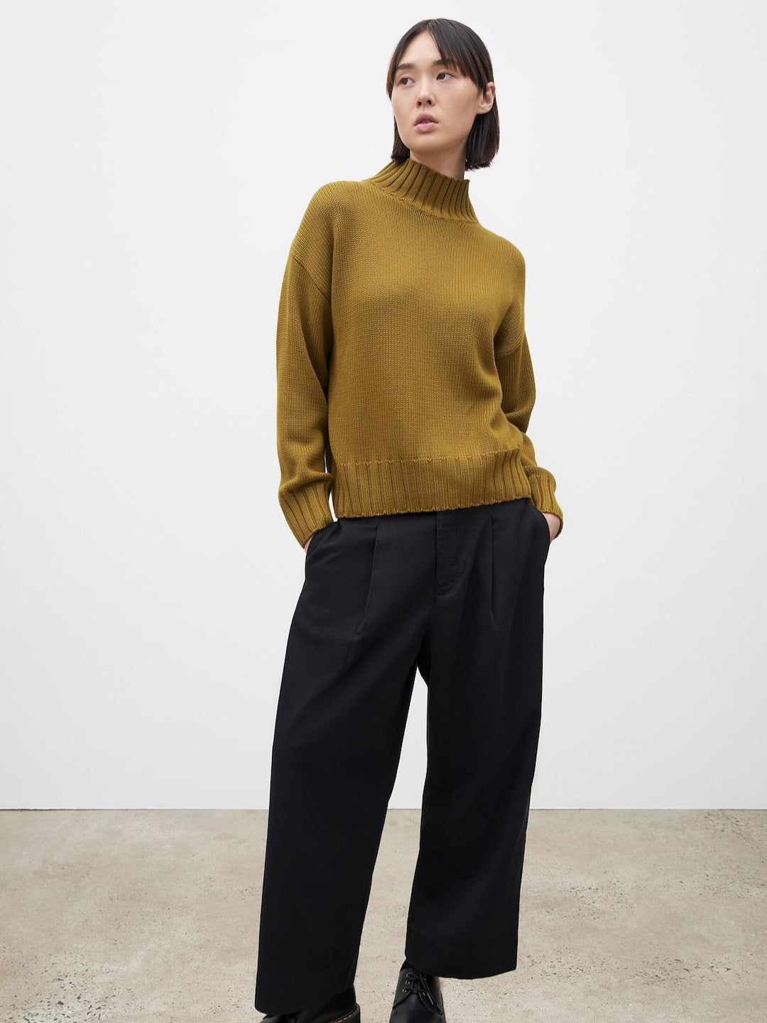 The model is wearing a Kowtow Chartreuse Staple Sweater and black wide leg pants.