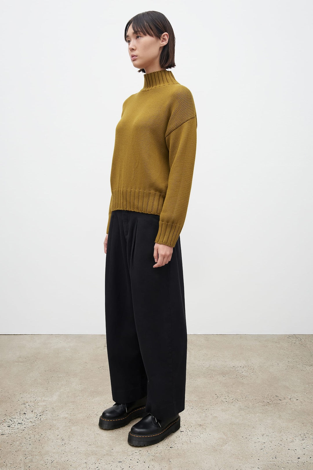 The model is wearing a Kowtow Staple Sweater – Chartreuse and black wide leg pants.
