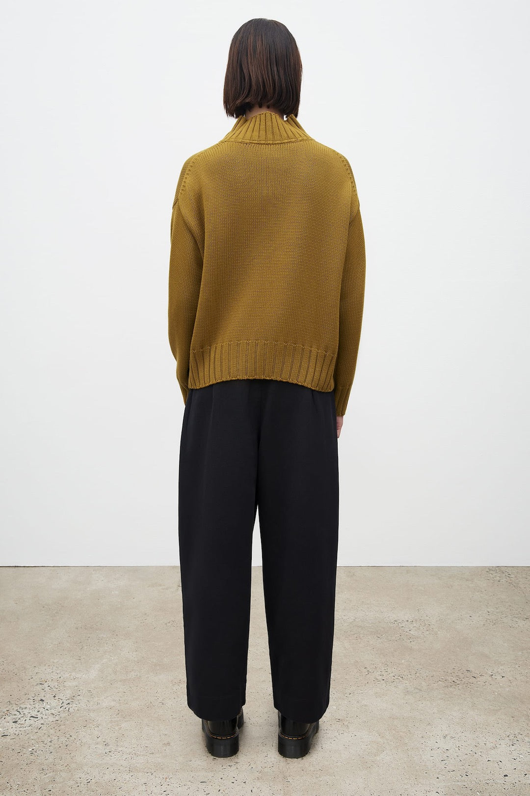 The back view of a woman wearing a Kowtow Staple Sweater – Chartreuse and black trousers.