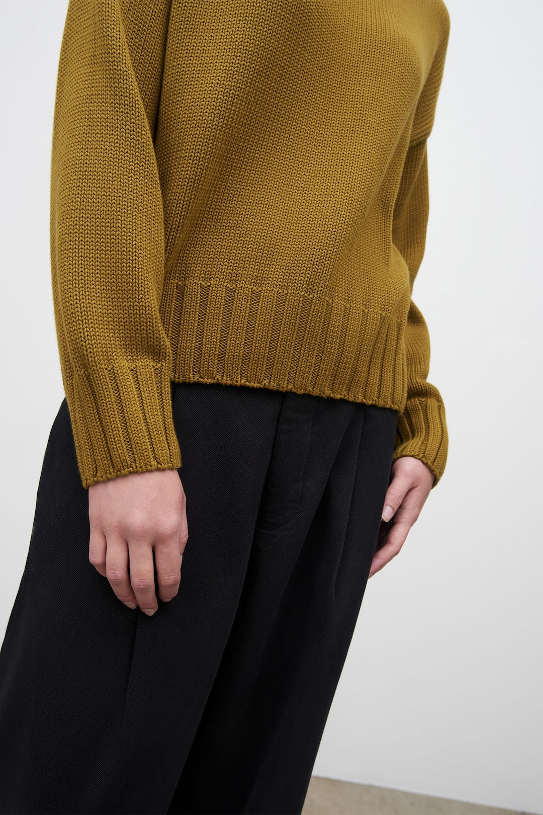 A woman wearing a Kowtow Staple Sweater – Chartreuse and black pants.