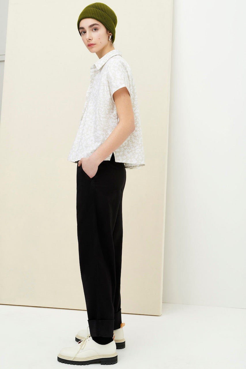 A woman in black trousers and a green beanie standing in front of a white wall wearing the Studio Shirt - Flora Print by Kowtow.