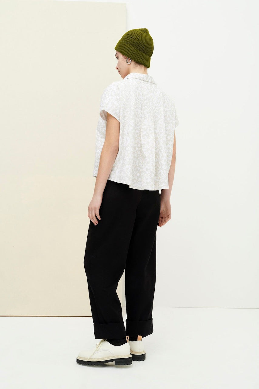 A woman wearing black pants and a green hat is now wearing the Studio Shirt - Flora Print by Kowtow.