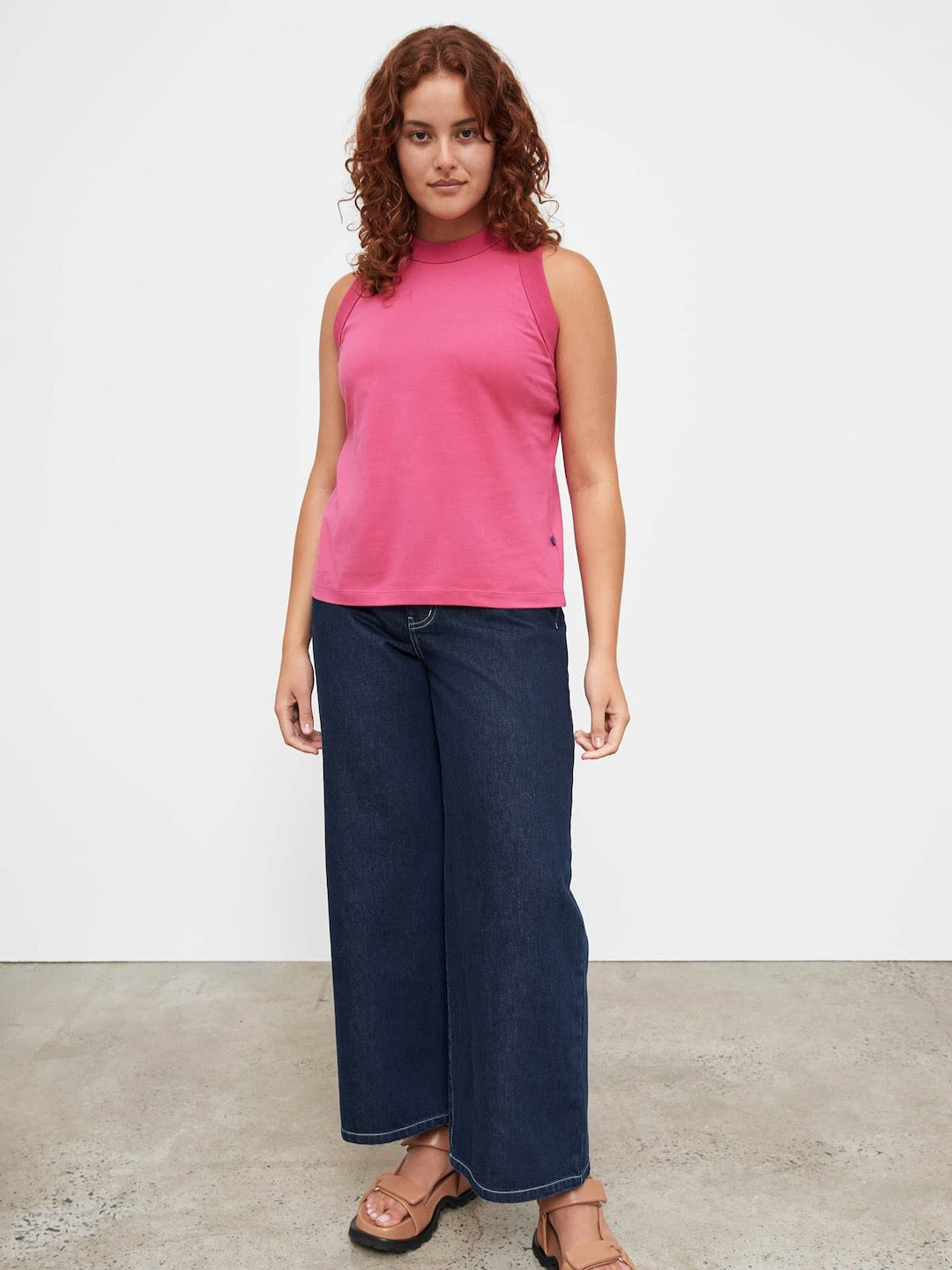 A woman wearing a Kowtow Fuchsia Tank Top and blue jeans.