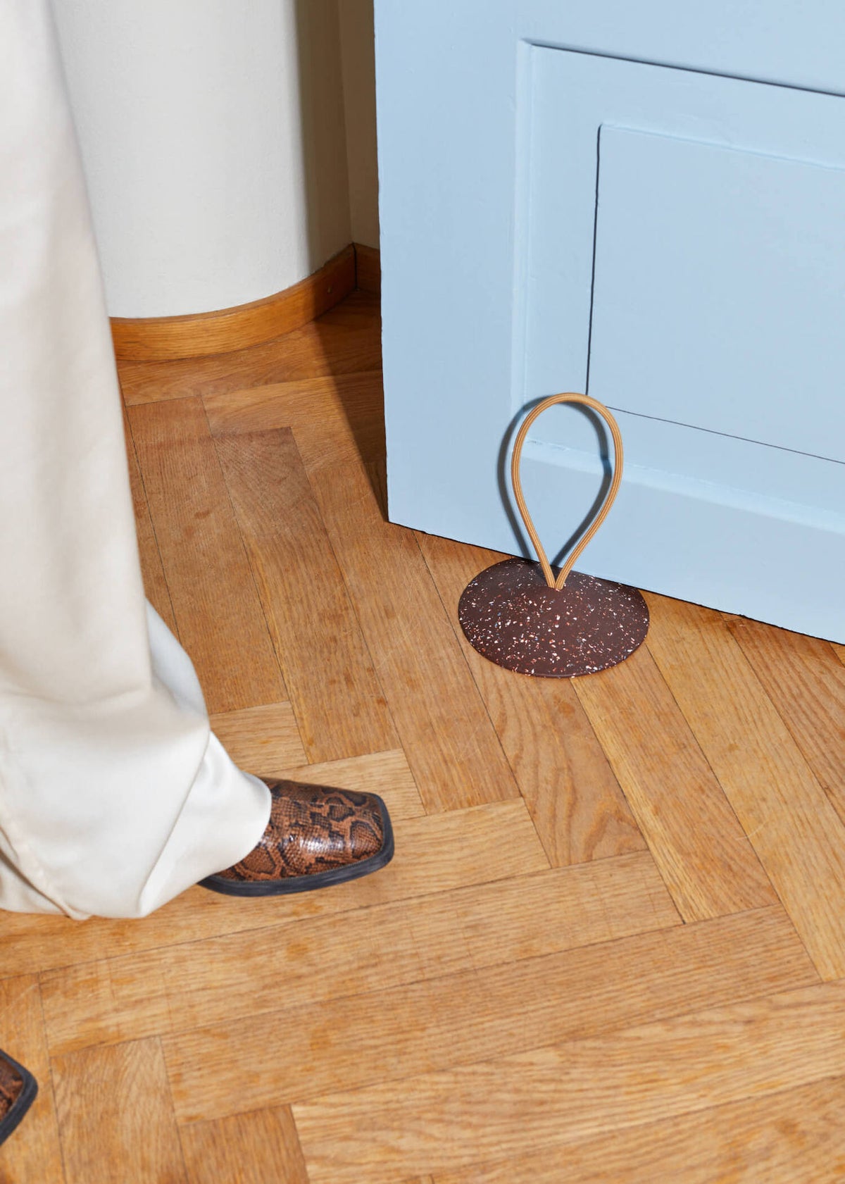 A person wearing a pair of brown Pidät STOP – Doorstop shoes standing next to a blue door.