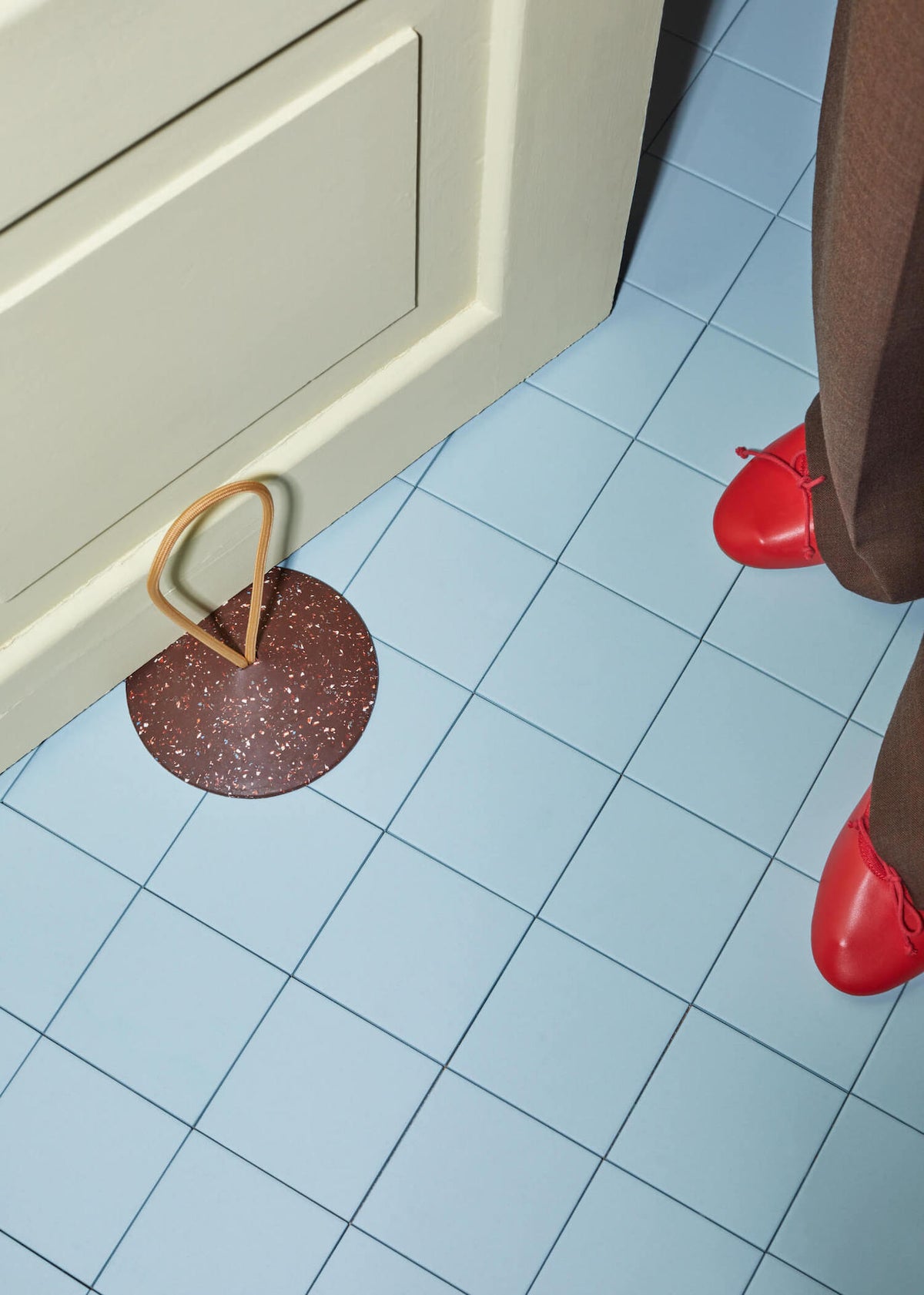 A person in red Pidät shoes standing on a tile floor with a STOP – Doorstop.