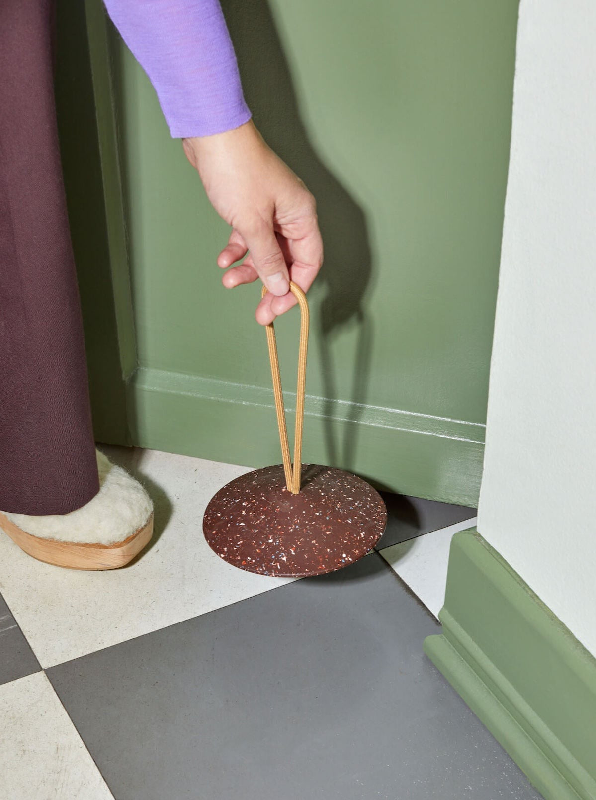 A person holding a Pidät wooden spoon on a tiled floor.