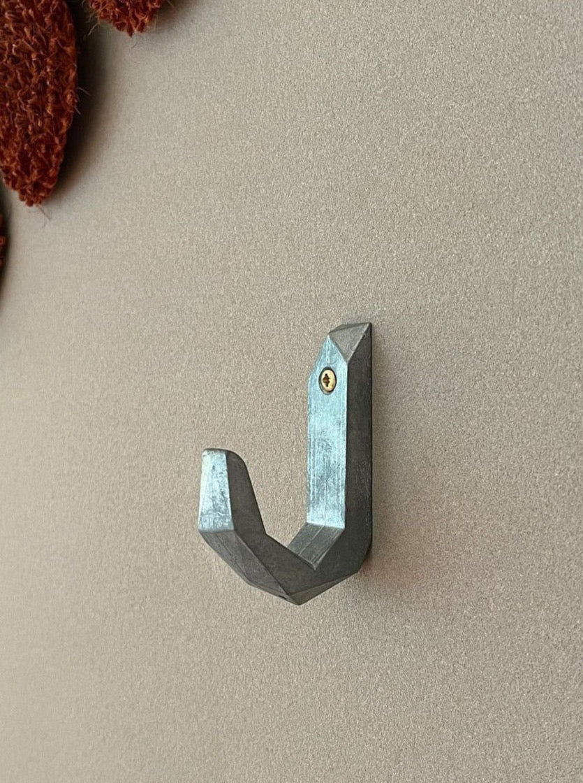 A Hookalotti metal hook, by Martino Gamper, hangs on a wall.
