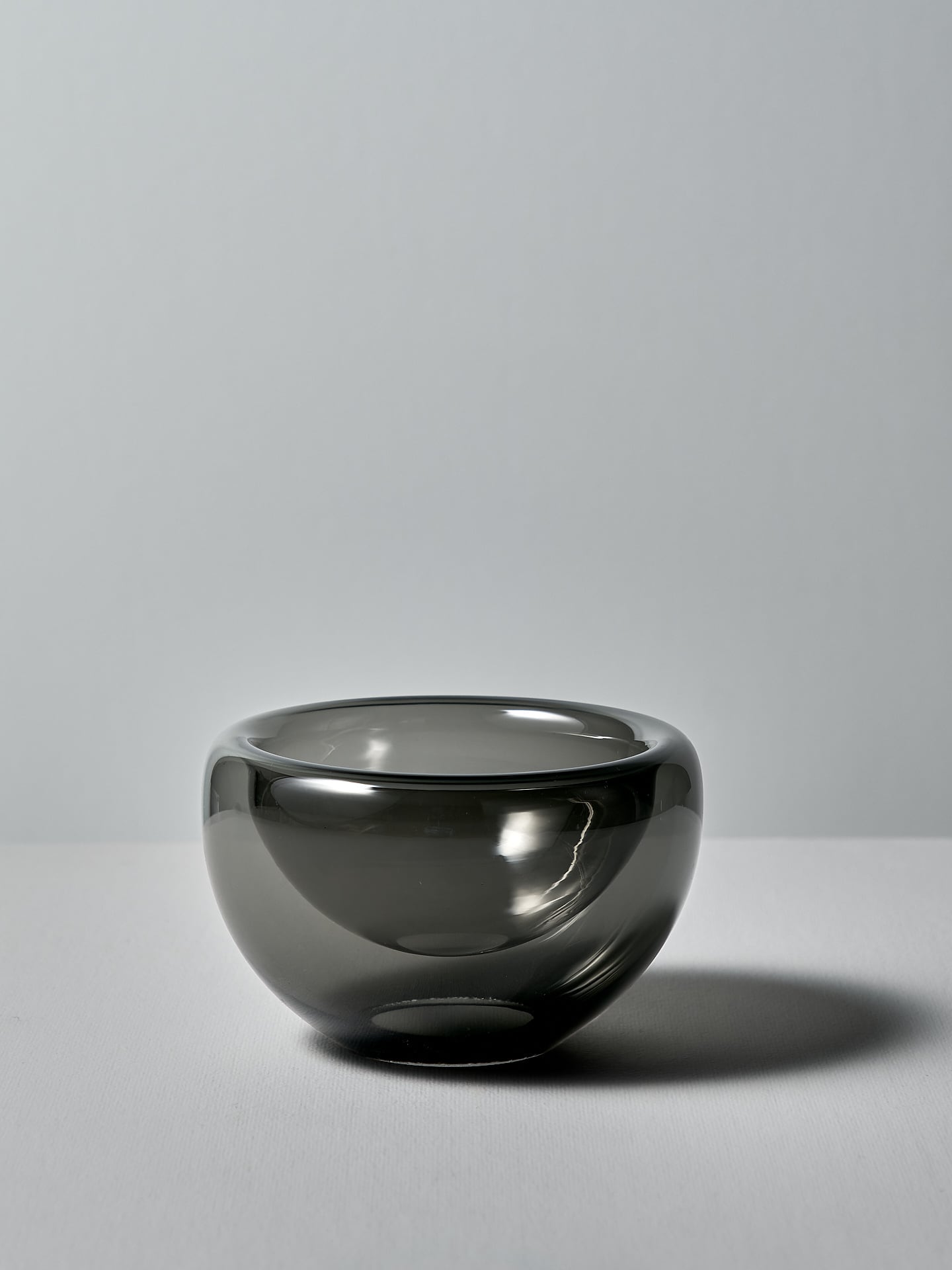 A Mini Fulvio Glass Bowl - Grey made by Matthew Hall sitting on a white table.