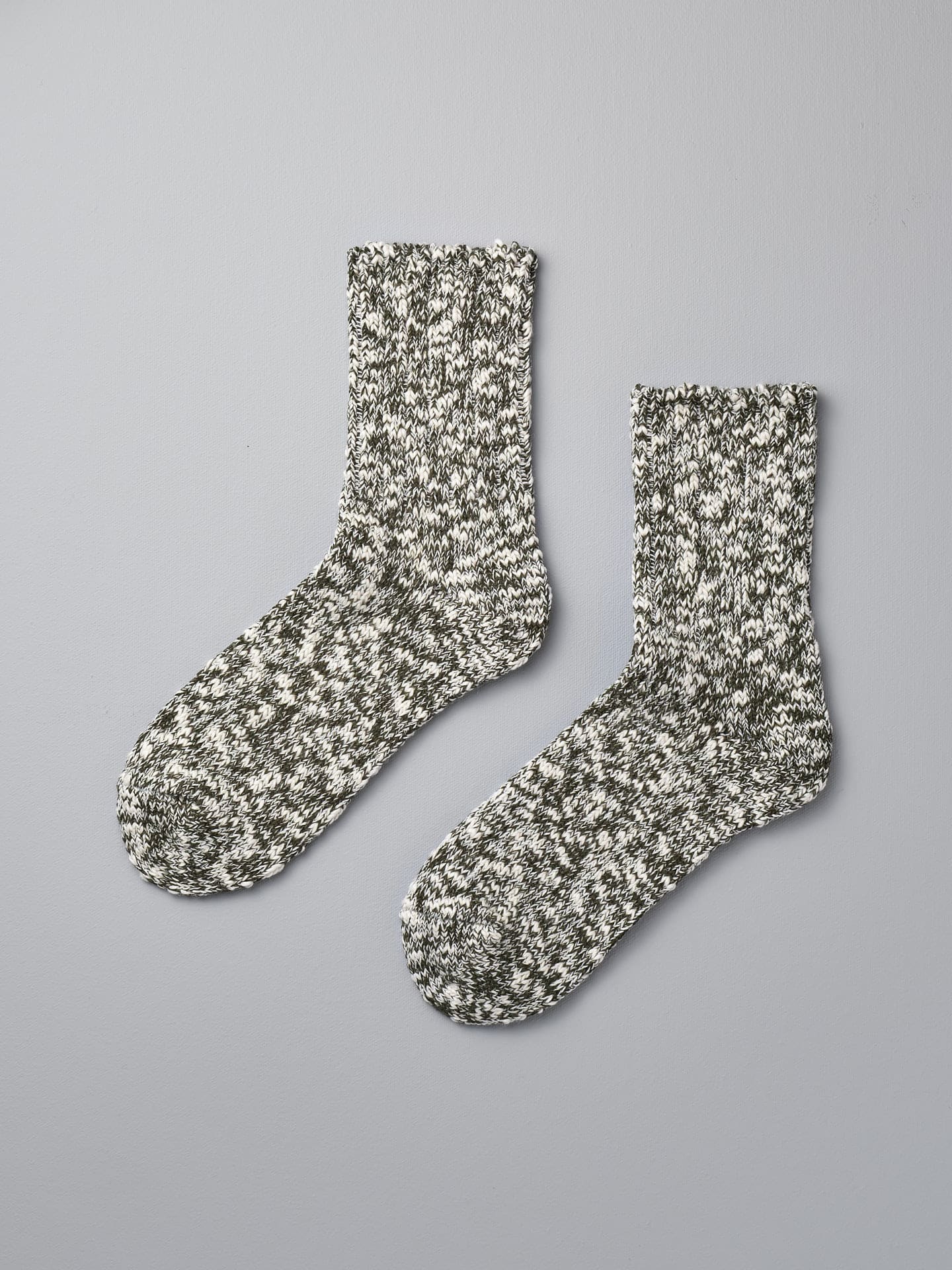 A pair of Japanese Slub Socks – Olive by Mauna Kea on a grey background.