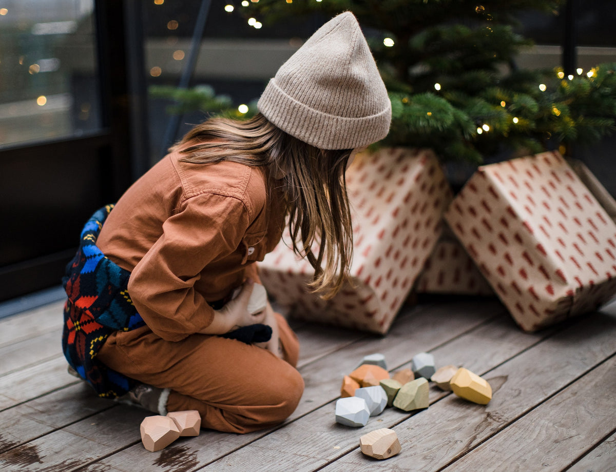 A little girl playing with Balancing Stones - Earthy by MinMin Copenhagen on the floor near a christmas tree.
