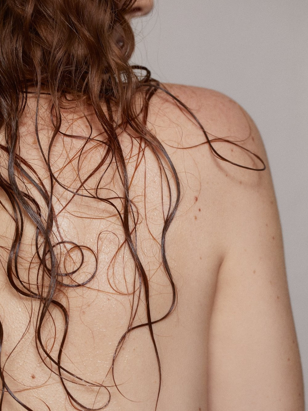 The back of a woman with long curly hair, sprayed with NOTO&#39;s Basil Yarrow Mist.