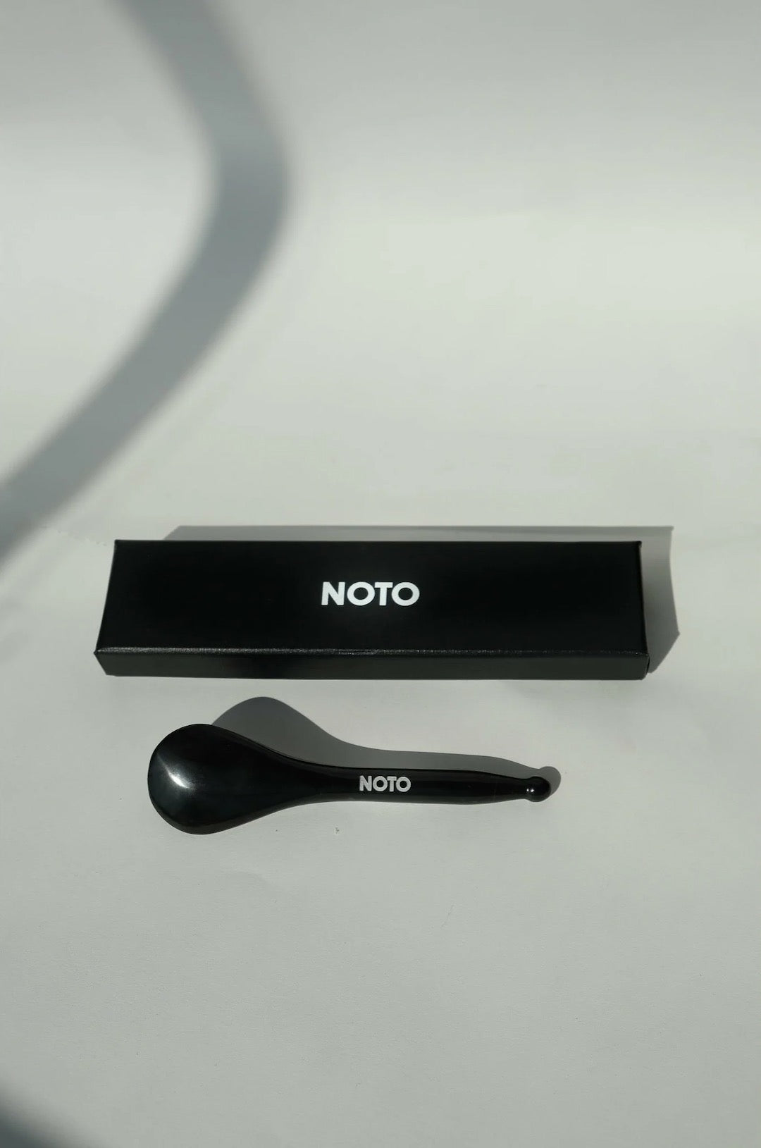 A black spoon with the word NOTO Bian Stone Facial Tool on it.