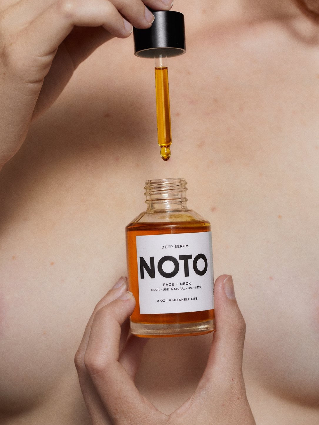A woman holding a bottle of Mini Deep Serum by NOTO on her breast.