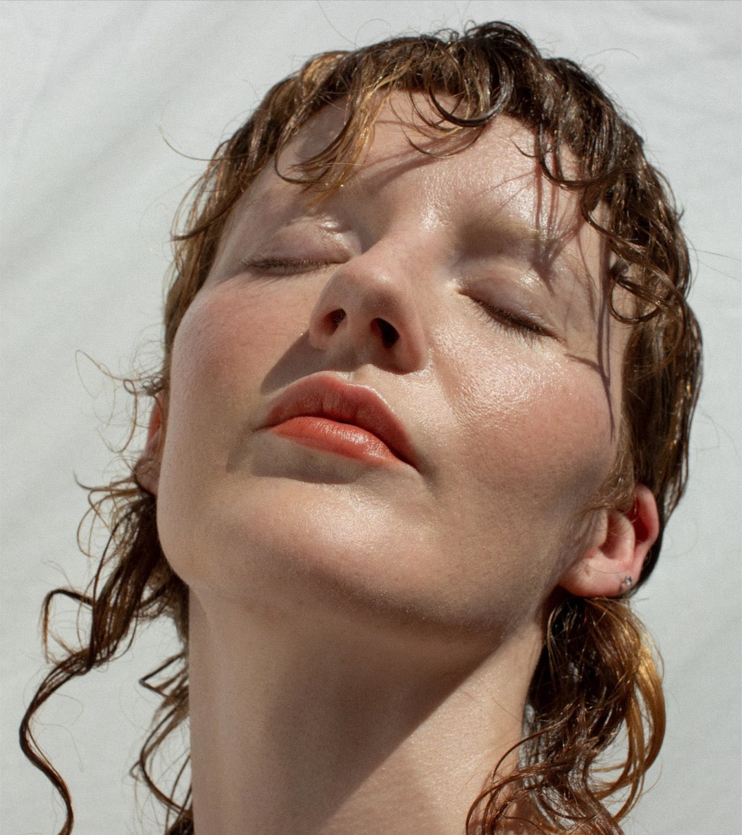 A woman with wet hair and eyes closed using the Ono Ono - Multi-Bene Stain Stick // Lips + Cheeks by NOTO.