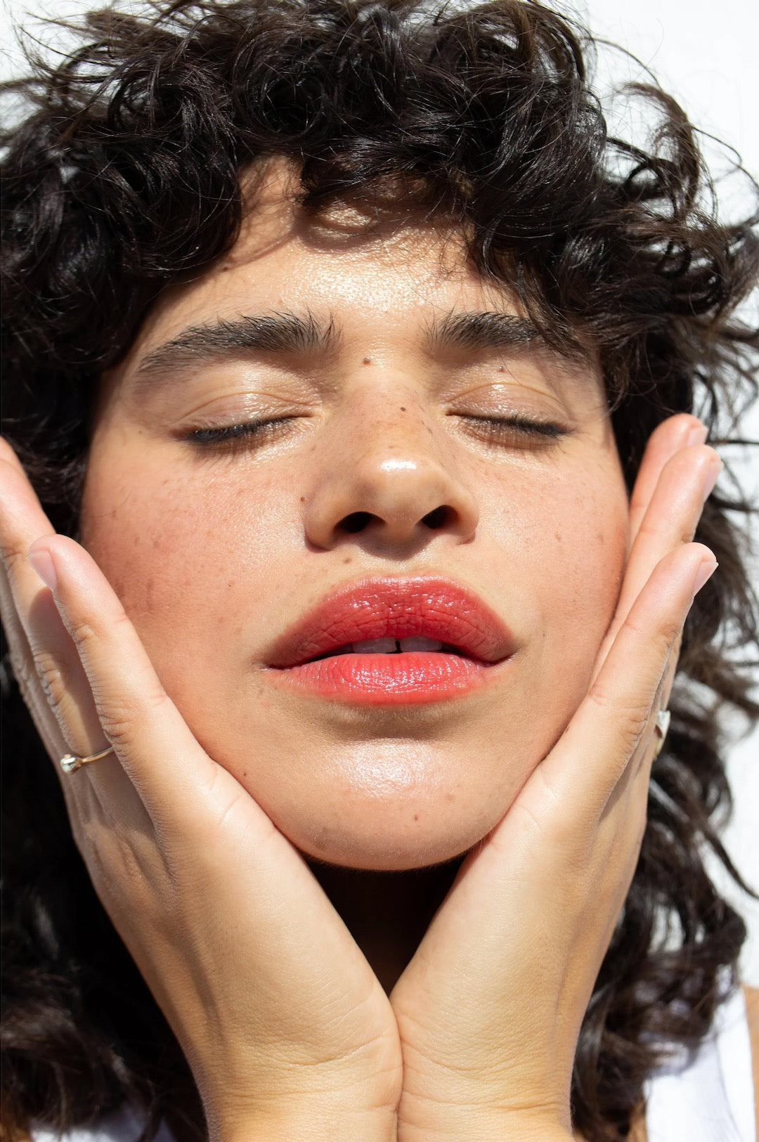 A woman with curly hair covering her face with her hands using the Oscillate – Multi-Bene Stain Stick // Lips + Cheeks by NOTO.