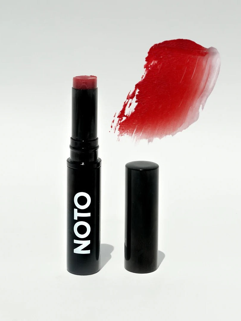 An Oscillate – Multi-Bene Stain Stick for Lips + Cheeks by NOTO with a red color and a black cap.