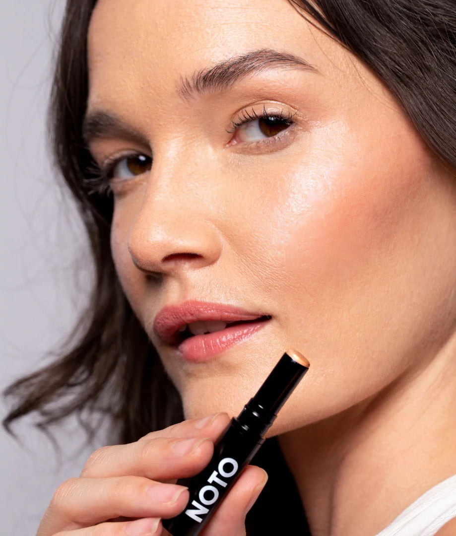 A woman is holding a NOTO Hydra Highlighter Stick // Face + Body in her hand.