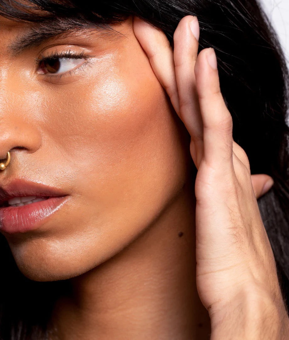 A woman with long hair and a piercing on her ear used the NOTO Hydra Highlighter Stick // Face + Body.