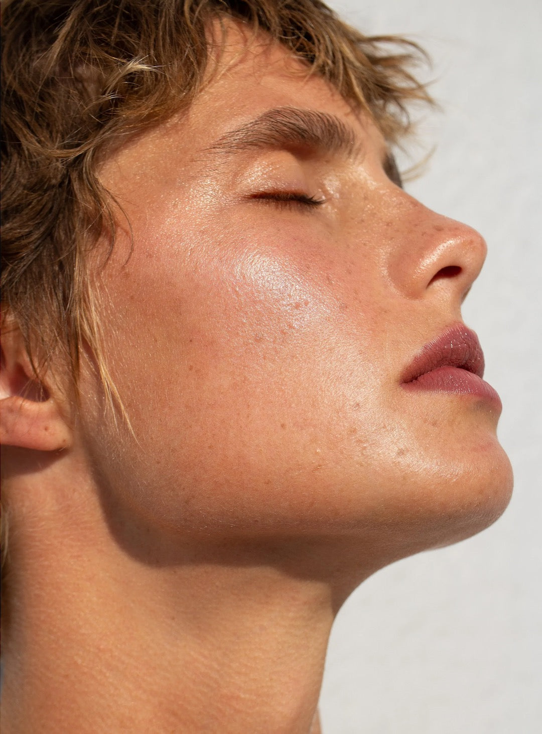 A man&#39;s face with his eyes closed using the NOTO Hydra Highlighter Stick for Face + Body.