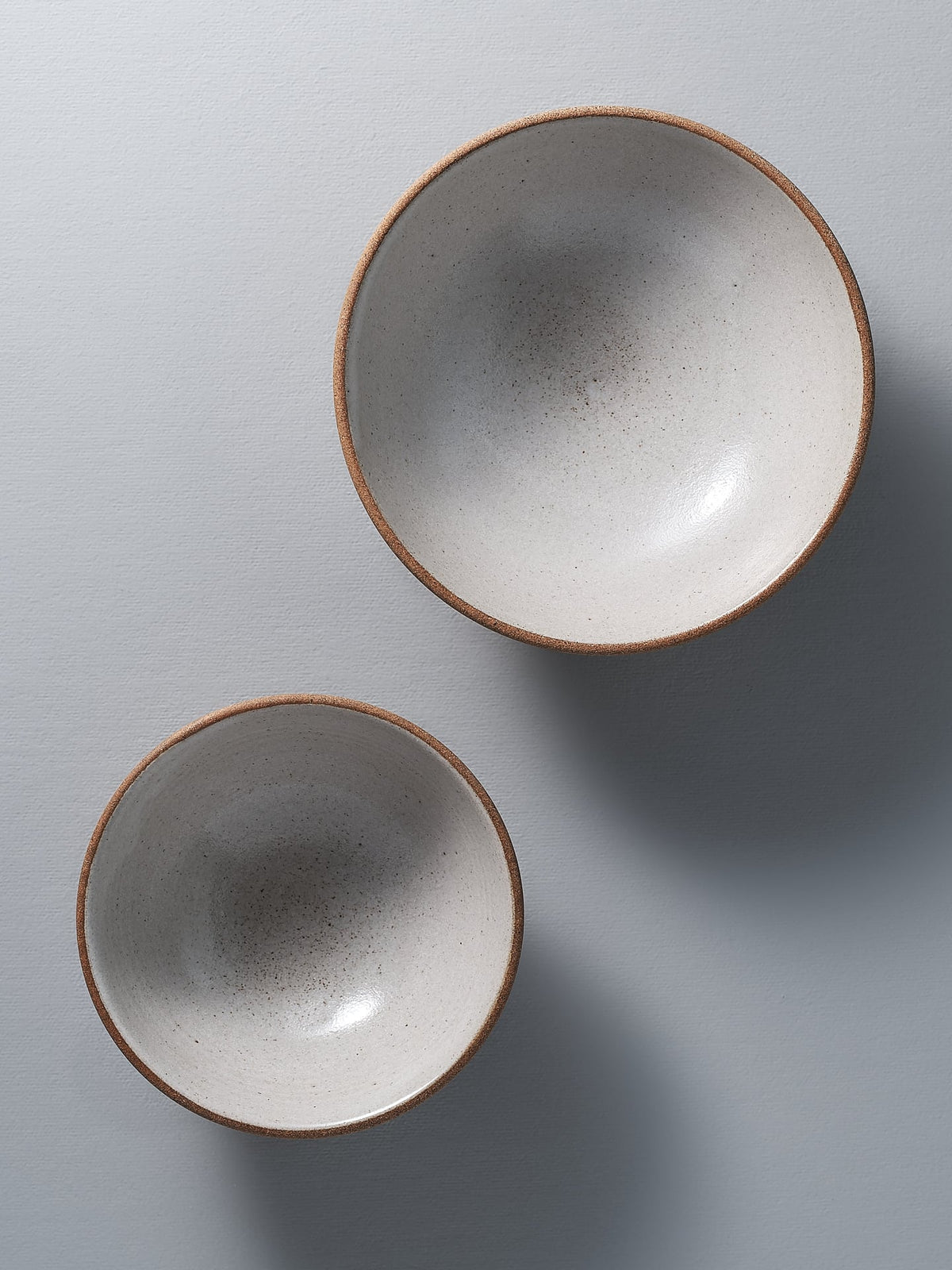 Two Nicola Shuttleworth Condiment Bowls – Small, white and brown, on a gray surface.