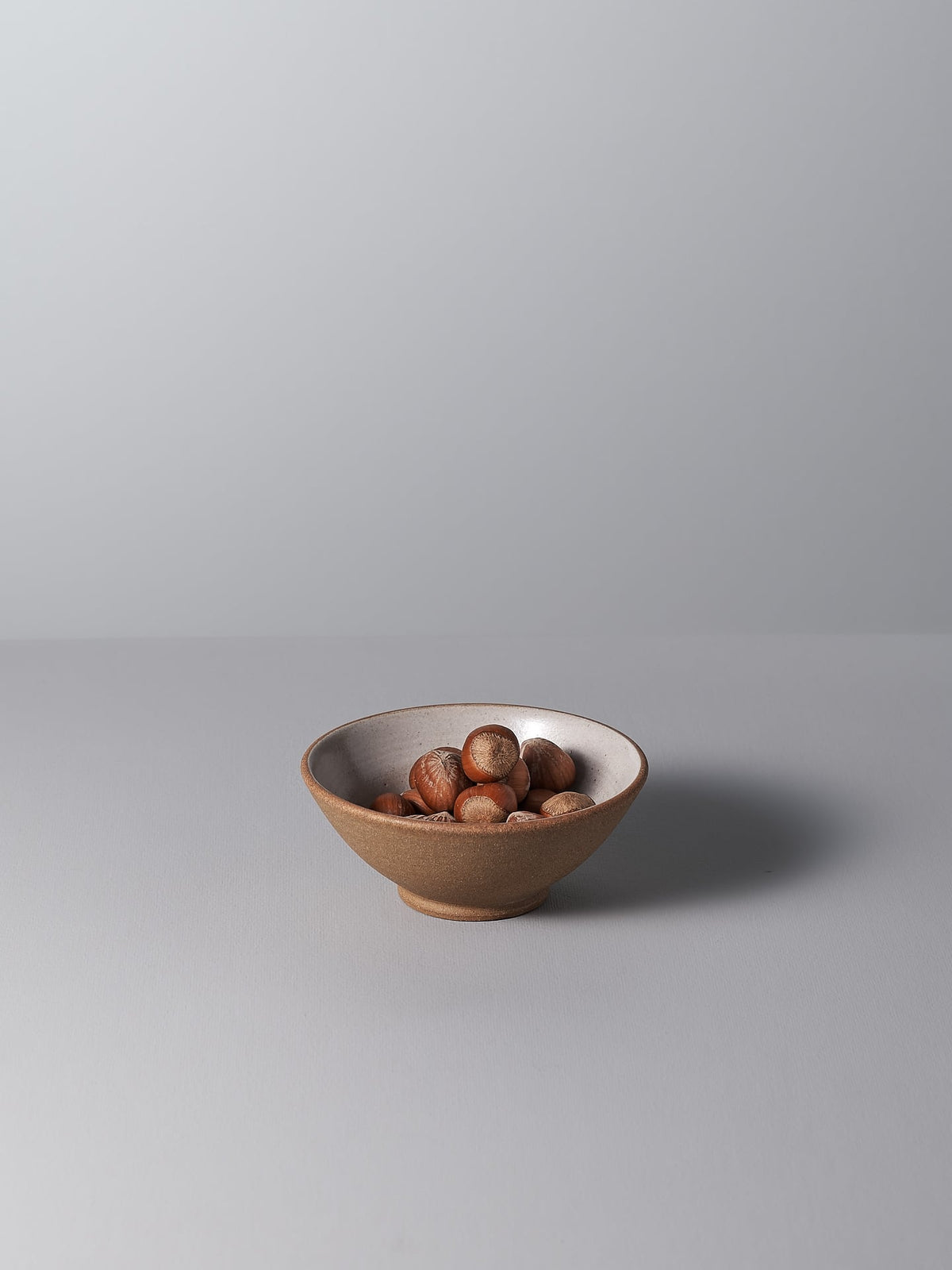 A Nicola Shuttleworth Condiment Bowl – Small filled with hazelnuts on a grey surface.