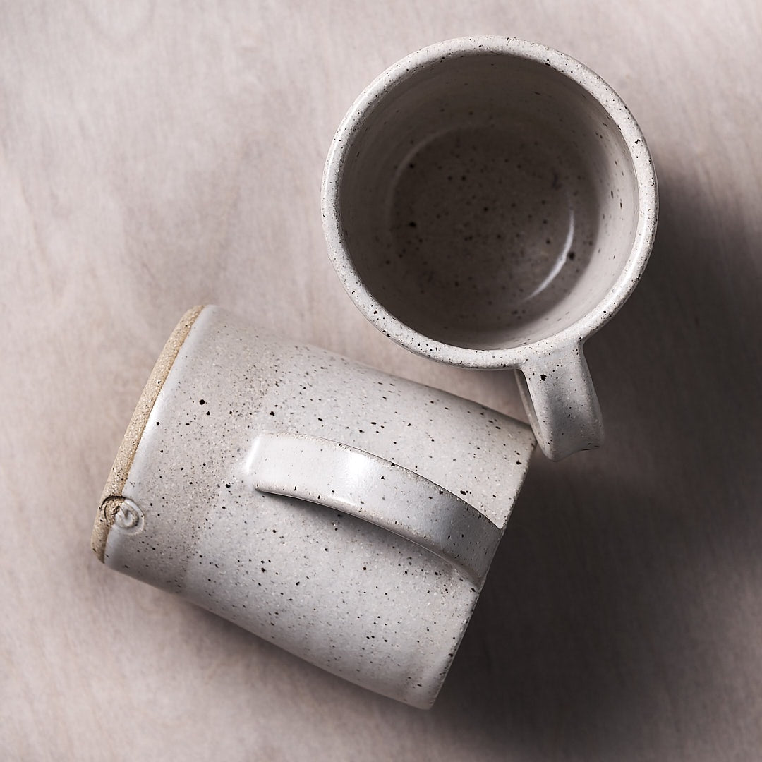 Two speckled mugs on a wooden surface.