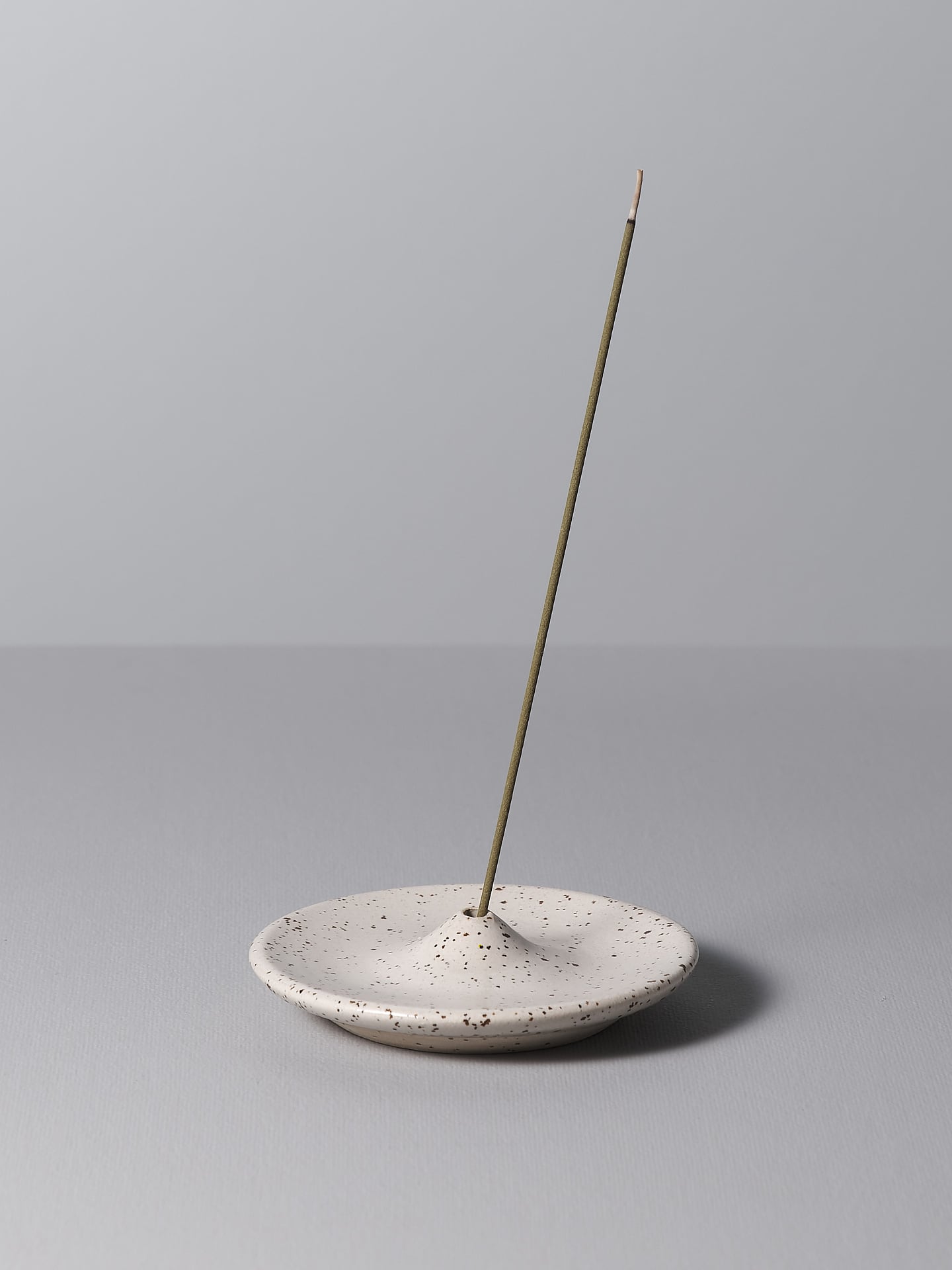 An Incense Holder - Speckled White by Nicola Shuttleworth on a white plate.