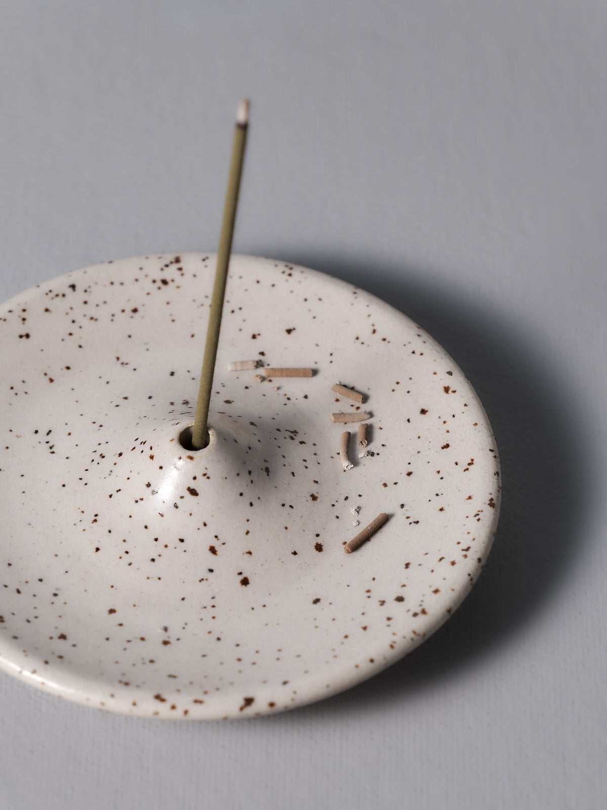 An Incense Holder – Speckled White with a stick sticking out of it, made by Nicola Shuttleworth.