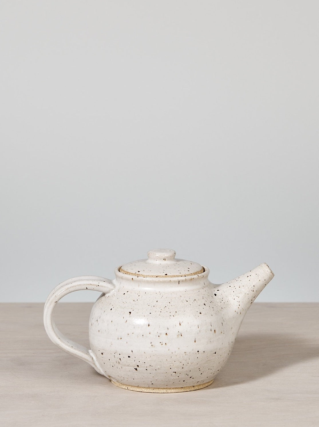 A handmade Nicola Shuttleworth Speckled Tea Pot sitting on a wooden table.