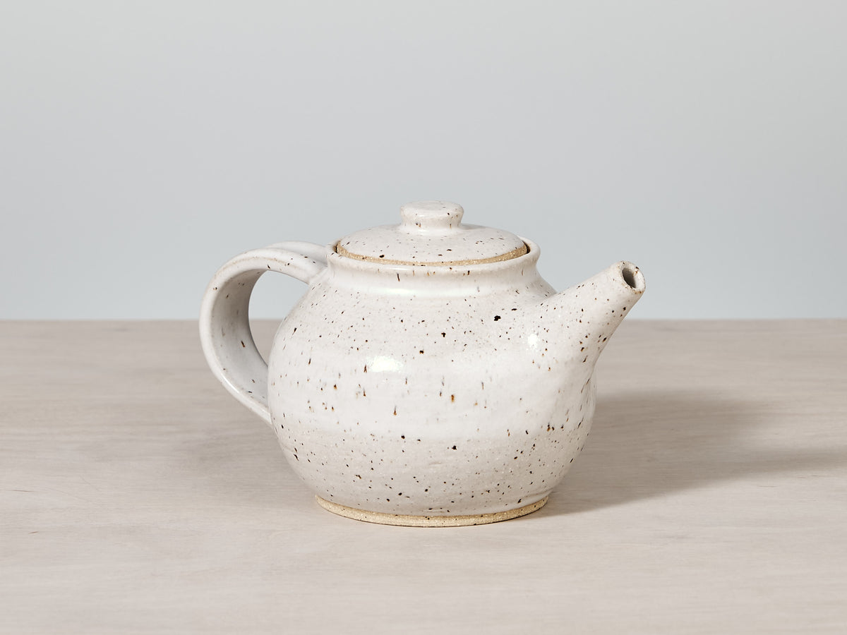 A handmade Nicola Shuttleworth white speckled teapot sitting on a wooden table in Wellington.