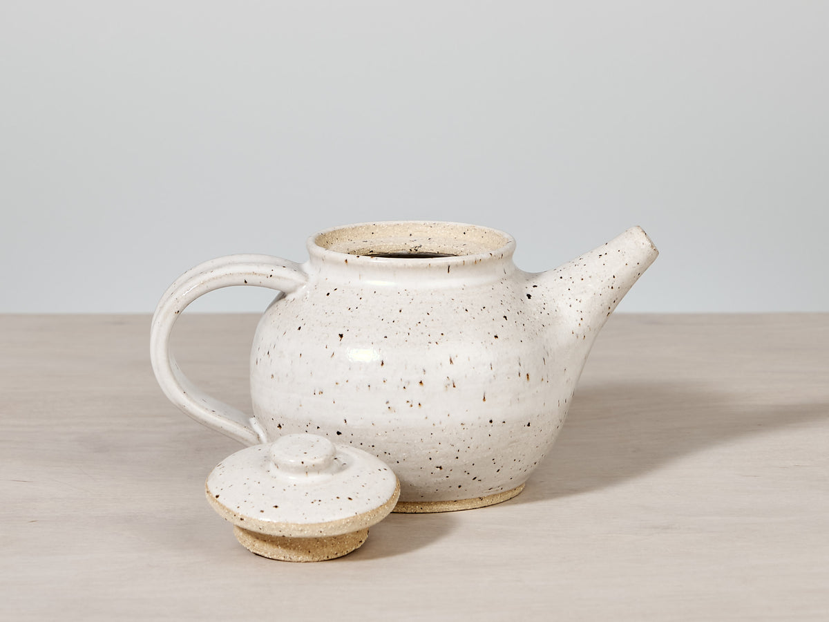 A handmade Nicola Shuttleworth speckled tea pot with a lid on a table.