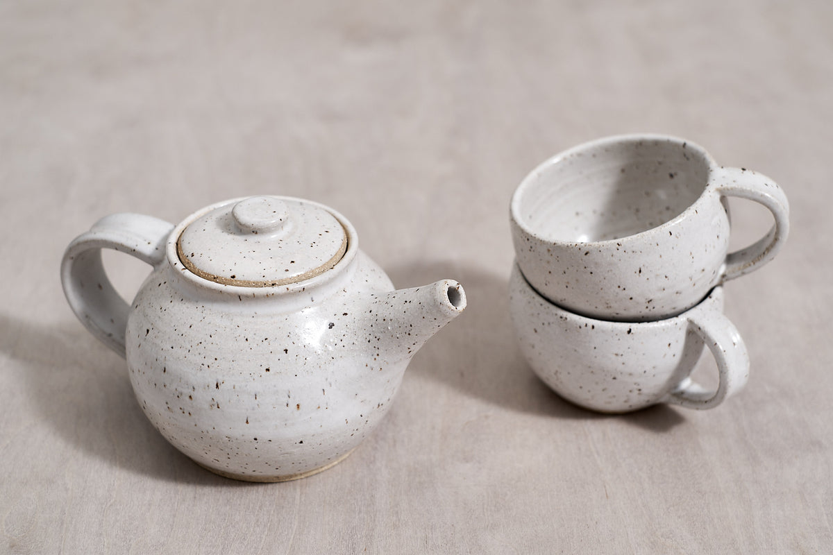 Two speckled tea pots and mugs on a wooden surface in Wellington.