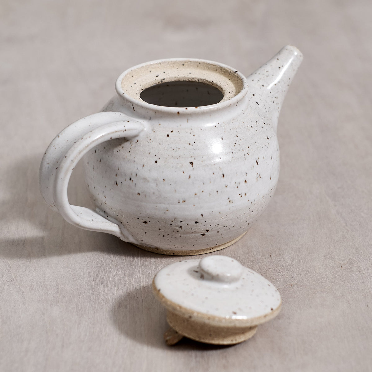 A handmade Nicola Shuttleworth Speckled teapot with a lid rests on a wooden table.