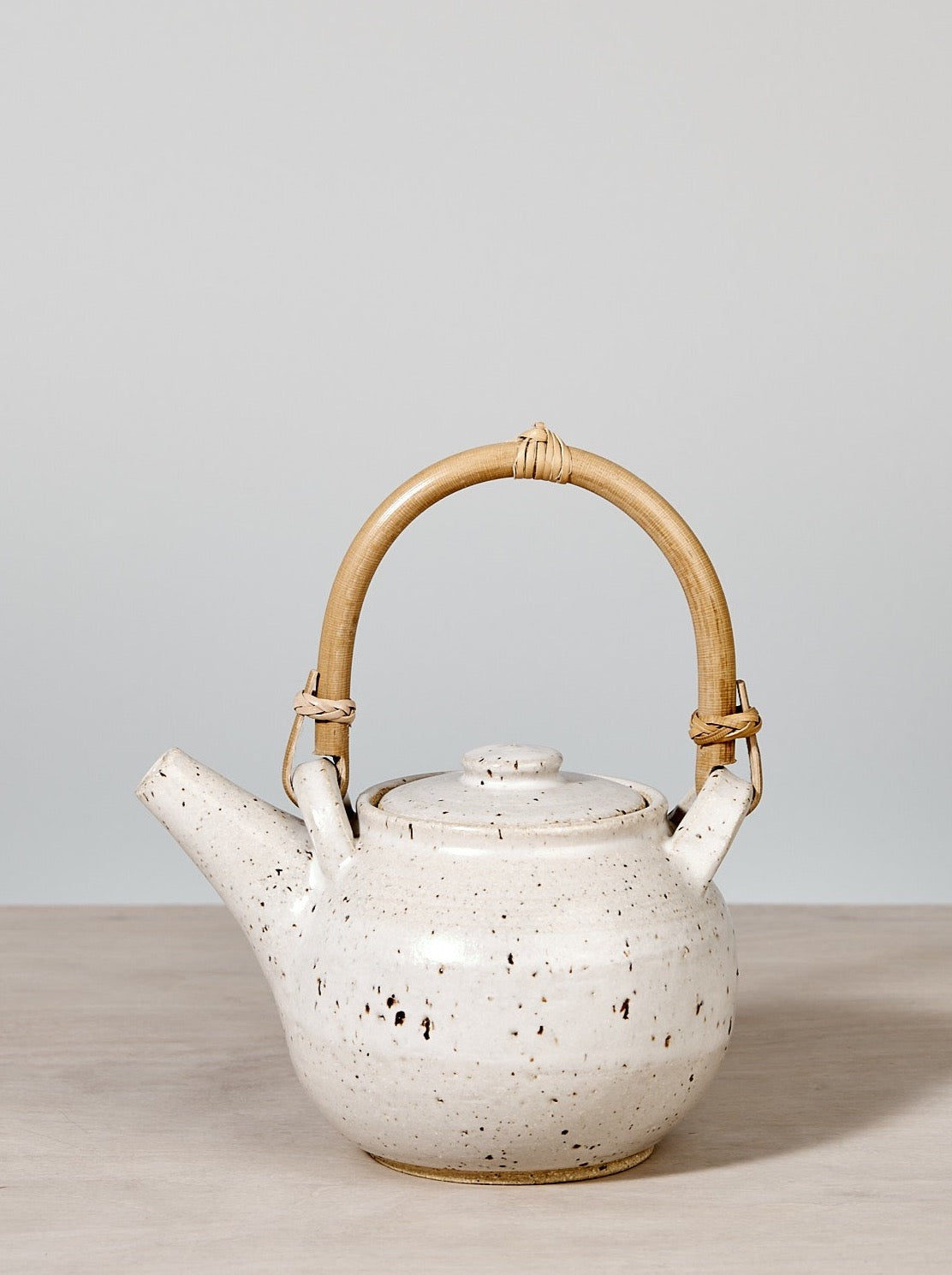 A Nicola Shuttleworth tea pot – speckled with Bamboo handle, on a wooden table.