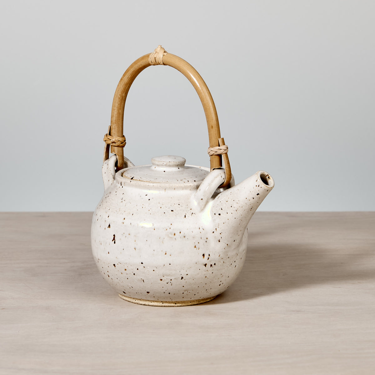 A handmade white Tea Pot - Speckled with Bamboo handle by Nicola Shuttleworth on a wooden table.