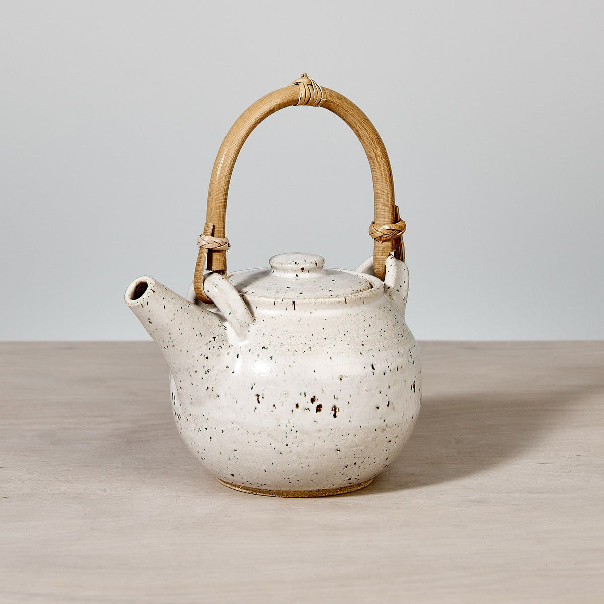 A Nicola Shuttleworth Speckled Tea Pot with a Bamboo handle on a wooden table.