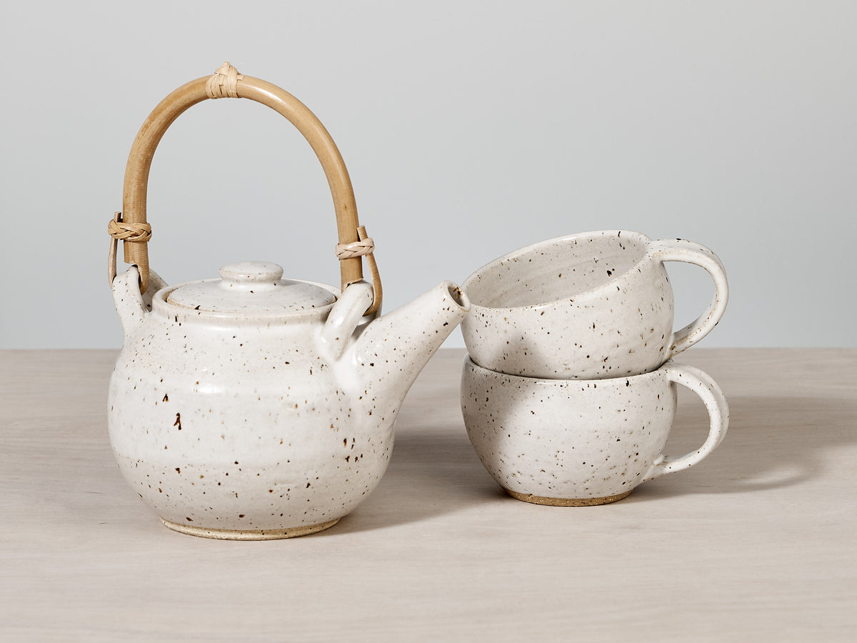 A handmade Nicola Shuttleworth Speckled Tea Pot with Bamboo handle and two mugs on a table.