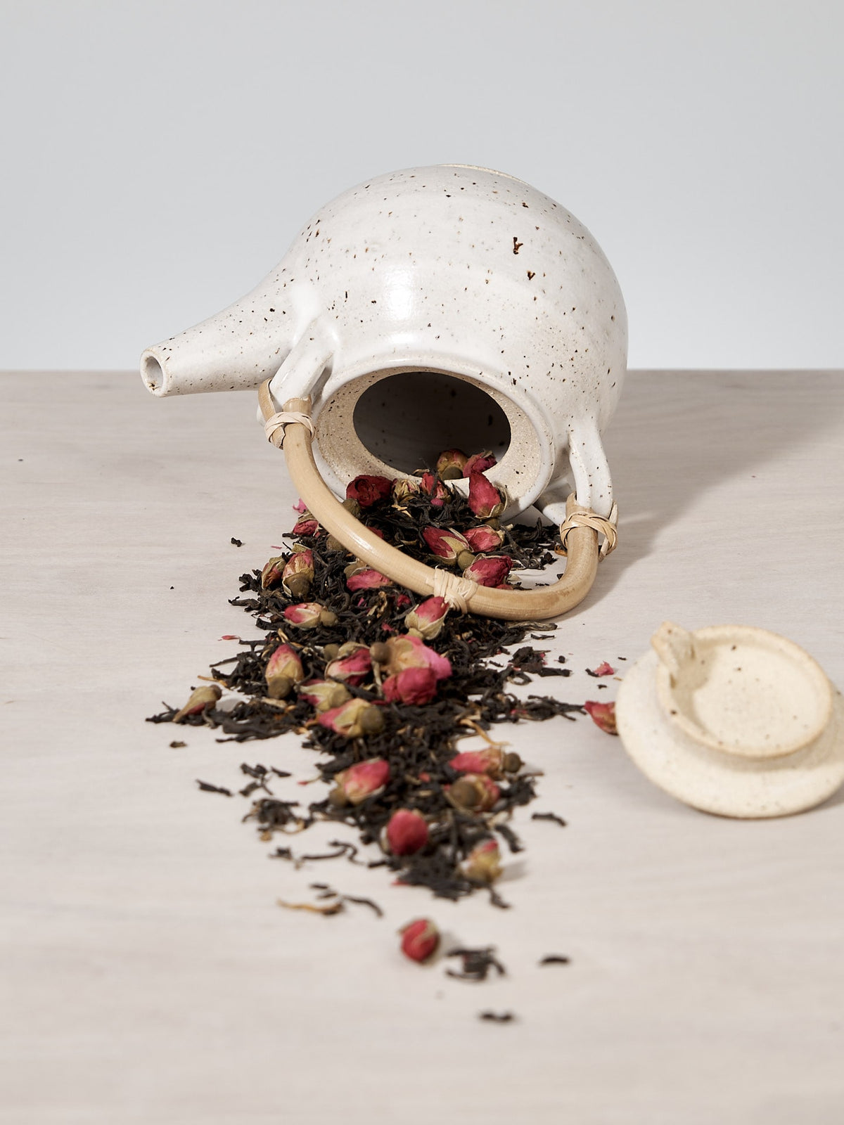A handmade Nicola Shuttleworth white teapot with rose petals on a table in Wellington.