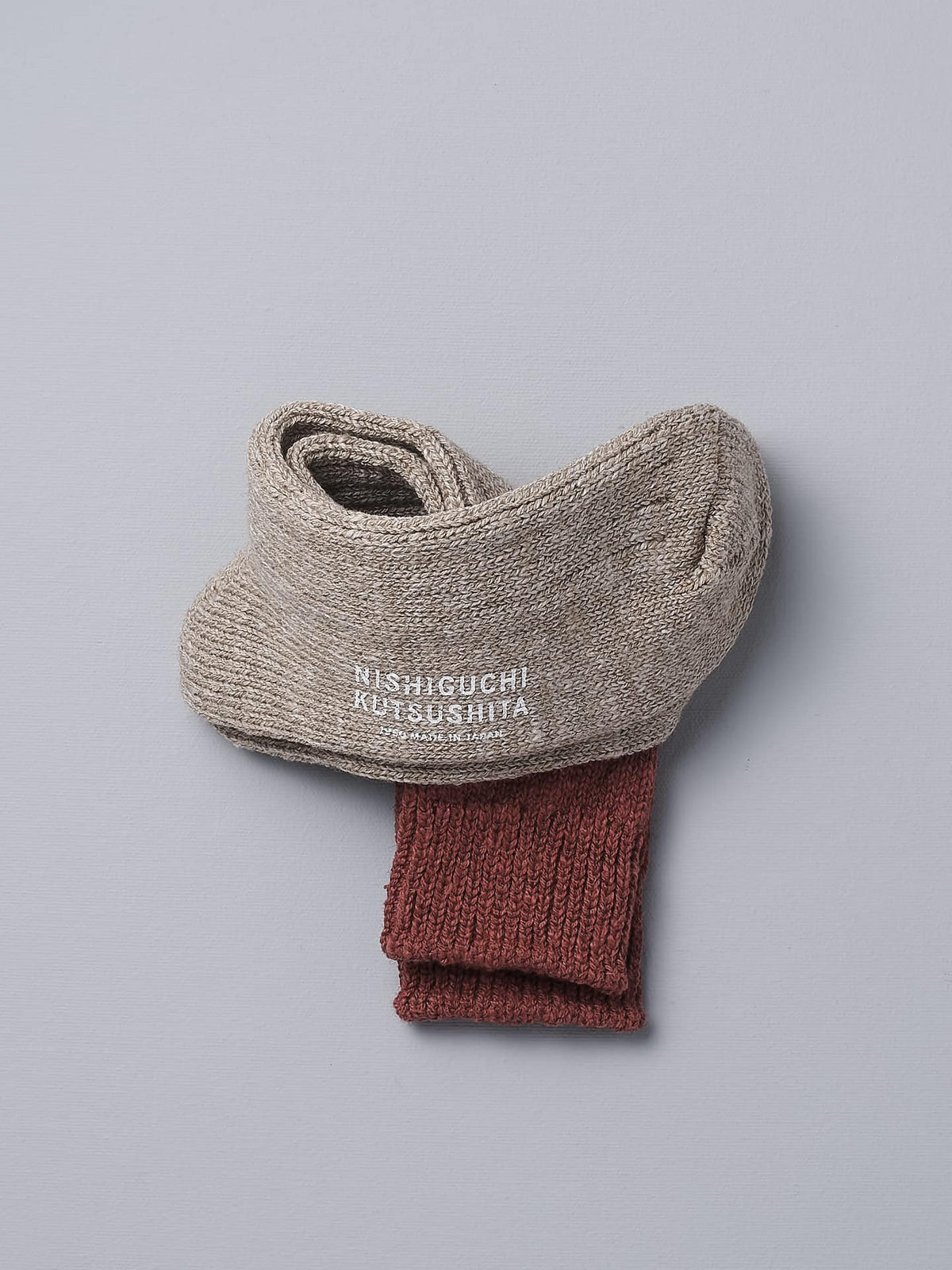 A pair of Boston Slab Socks – Red Brick by Nishiguchi Kutsushita on a grey surface.