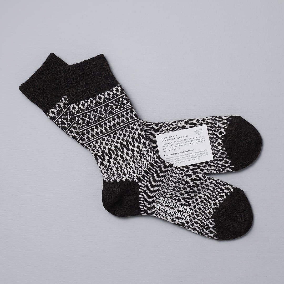 A pair of Oslo Wool Jacquard Socks – Coffee by Nishiguchi Kutsushita on a grey surface.