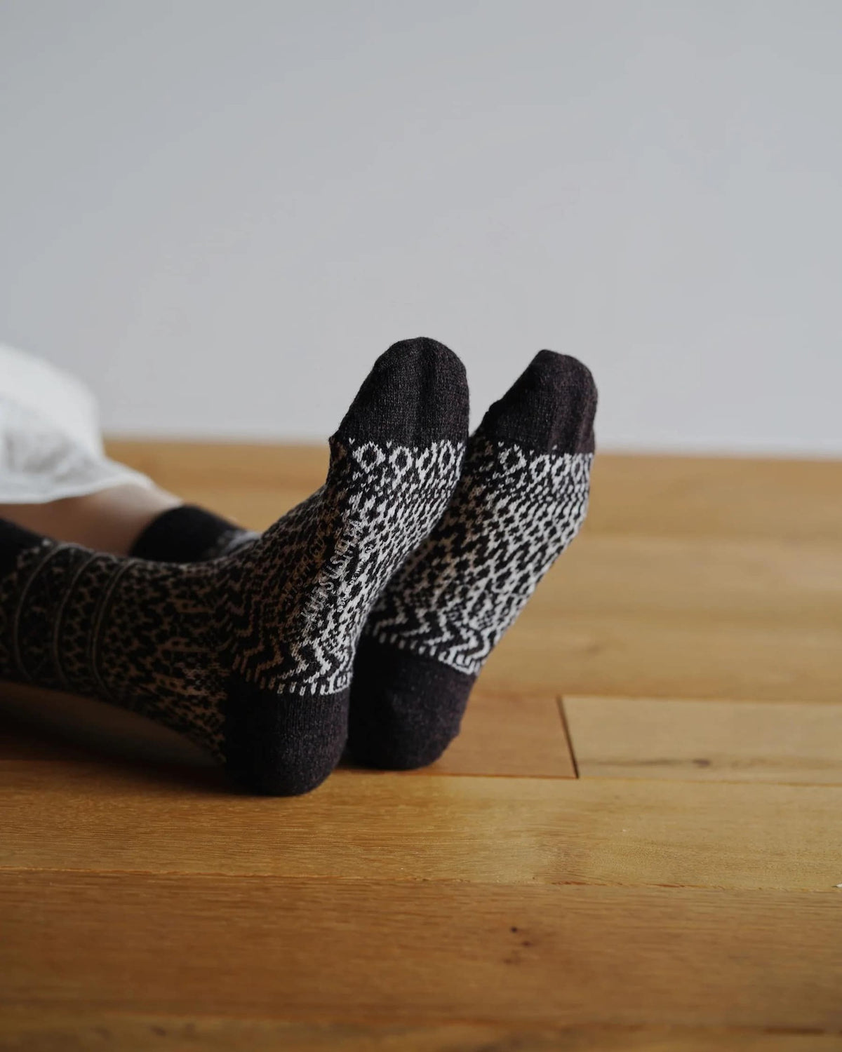 A pair of Oslo Wool Jacquard Socks – Coffee by Nishiguchi Kutsushita, laying on a wooden floor.