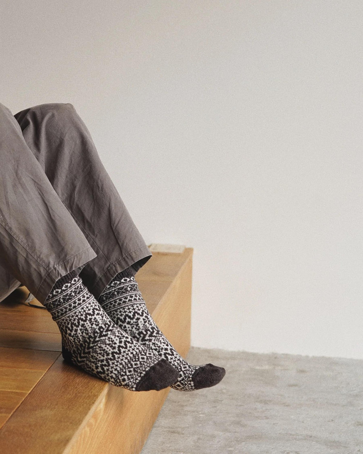 A person sitting on a wooden bench wearing Nishiguchi Kutsushita Oslo Wool Jacquard Socks – Coffee.
