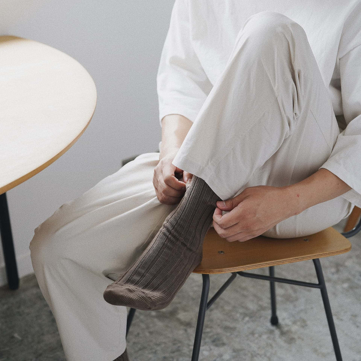 A man sitting on a chair wearing a pair of Nishiguchi Kutsushita Praha Cotton Socks – Chocolate Milk.