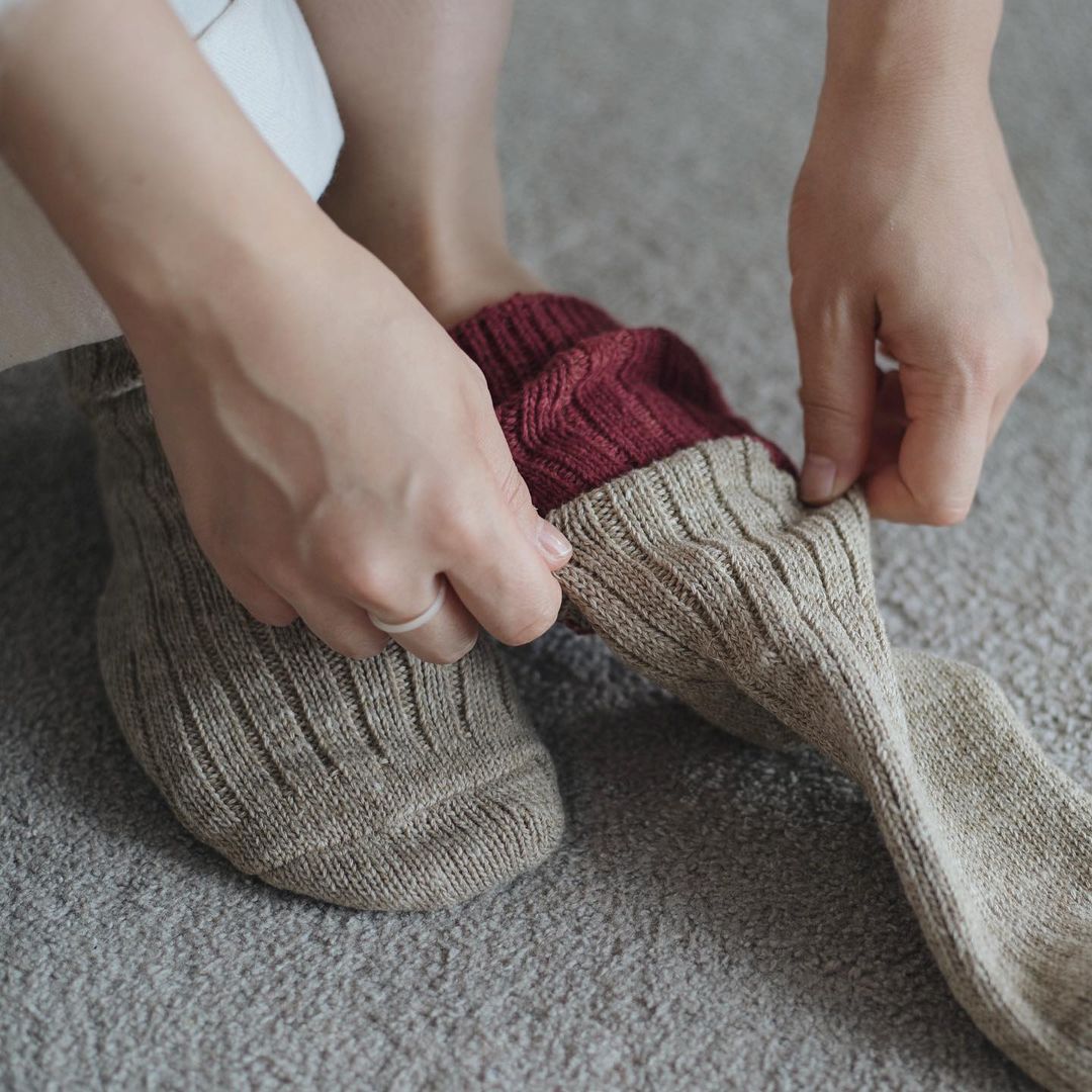 A person putting on a pair of Boston Slab Socks – Red Brick, made by Nishiguchi Kutsushita.