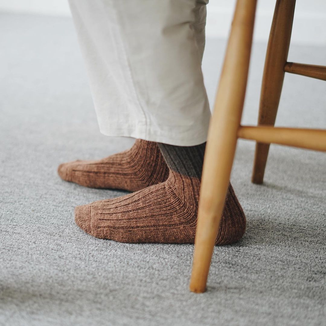 A person wearing Boston Slab Socks – Brown Fawn by Nishiguchi Kutsushita on a chair.