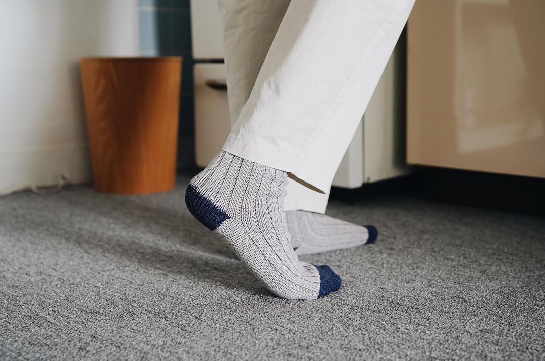 A person standing in a kitchen wearing Boston Slab Socks – Grey Denim by Nishiguchi Kutsushita.