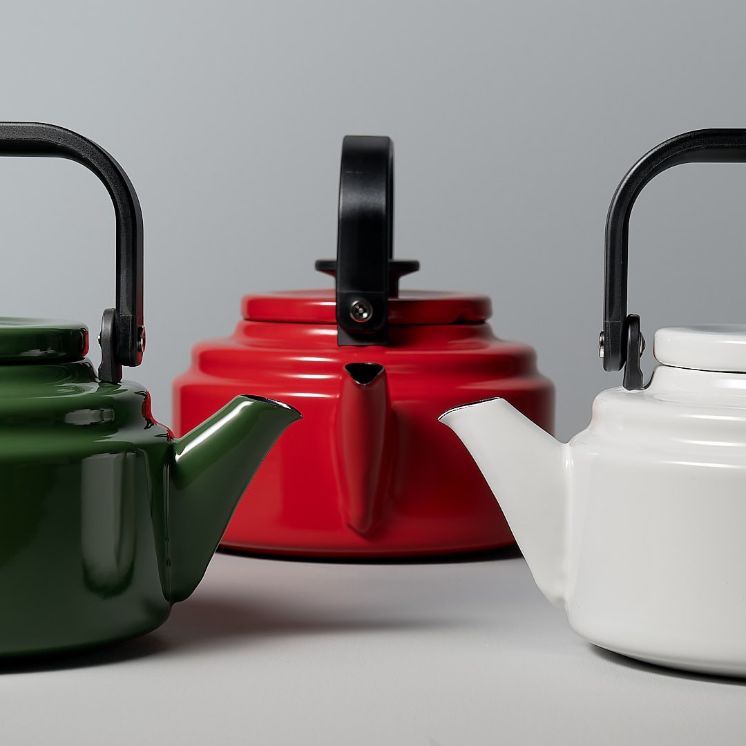 Three Amu Stove-top Kettles in three colours, Green, Red and White. By Noda Horo, on a grey background.